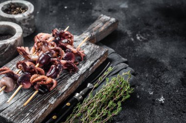 Skewers with Grilled baby mini octopuses. Black background. Top view. Copy space.