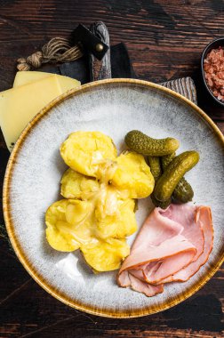 Eritilmiş Raclette İsviçre peyniri, haşlanmış patates ve jambon. Ahşap arka plan. Üst görünüm.