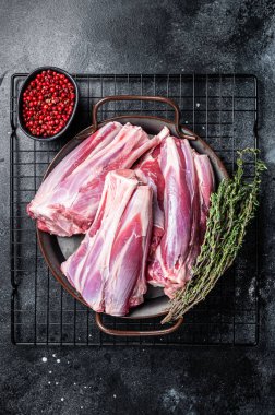 Raw lamb leg shanks in a steel tray with herbs. Black background. Top view.