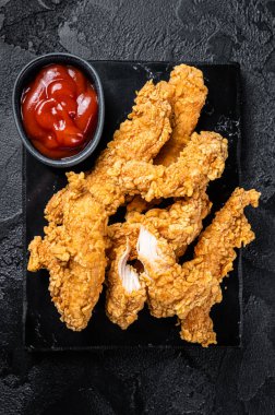 Breaded chicken strips Fingers with Ketchup. Black background. Top view.