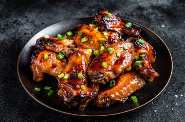 Baked chicken wings with sweet chili sauce in a plate. Black background. Top view.