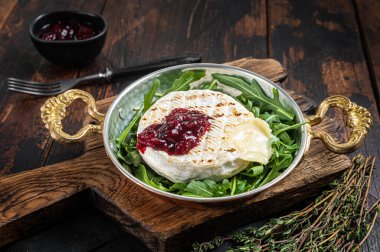 Kızılcık soslu kamembert peyniri ve tavada roka salatası ile süslenmiş. Ahşap arka plan. Üst görünüm.
