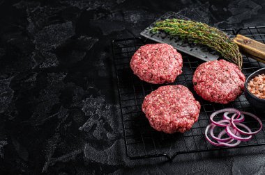 Raw minced beef cutlets with spices and herbs ready for cooking. Black background. Top view. Space for text.