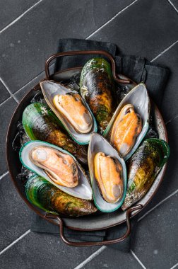 Large green mussels in shells on tray with ice. Black background. Top view.