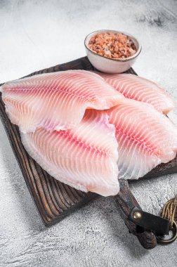 Çiğ beyaz tilapia balığı, pişirilmemiş fileto mutfak tepsisinde şifalı otlar. Gri arka plan. Üst görünüm.