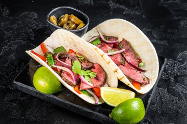 Mexican Steak Tacos with beef meat, cilantro, green sauce, jalapenos and onion. Black background. top view.