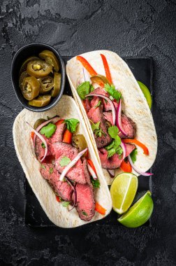 Mexican Steak Tacos with beef meat, cilantro, green sauce, jalapenos and onion. Black background. top view.