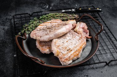 Grilled delicious pork chop steaks with herbs and spices. Black background. Top view.