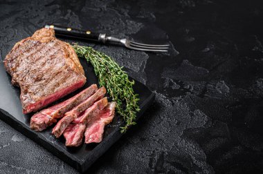 Griiled on BBQ sliced Striploin marbled beef meat steak. Black background. Top view. Copy space.