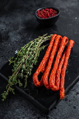 Smoked kabanos sausages with herbs on marble board. Black background. Top view.