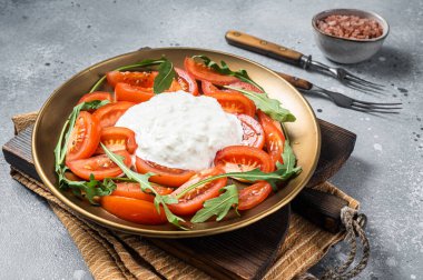 İtalyan peynirli stracciatella burrata tabakta taze domates ve roka. Gri arka plan. Üst görünüm.