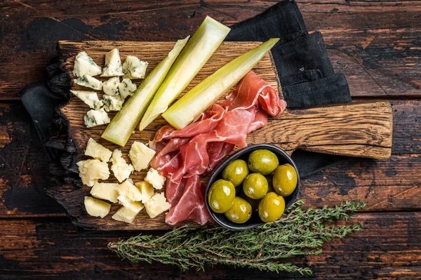 Cheese and meat plate, antipasti with Prosciutto ham, Parmesan, Blue cheese, Melon and Olives on wooden board. Wooden background. Top view.