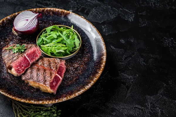 Grilled Oyster Top Blade beef meat steak on a plate with salad. Black background. Top View. Copy space.