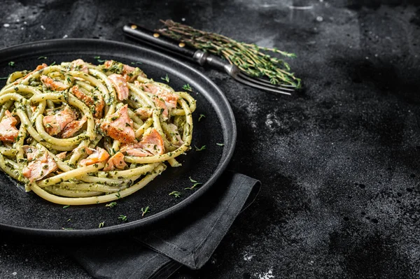 Bucatini Pasta with Smoked Salmon fillet and creamy spinach. Black background. Top view. Copy space.