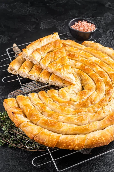 Turkish Tepsi Boregi, Round Borek cheese pie on kitchen board. Black background. Top view.