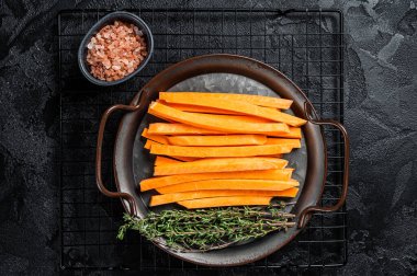 Sliced Sweet potatoes in a steel tray, fresh batata fries ready for cooking. Black background. Top view.
