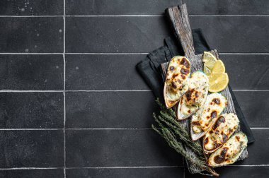 Mussels in Roquefort cheese sauce in shells on wooden board. Black background. Top view. Copy space.