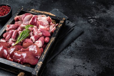 Uncooked Bird offals, raw chicken giblets, gizzards, stomachs, liver and hearts in a wooden tray. Black background. Top view. Copy space.