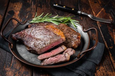 Grilled picanha or top sirloin beef steak with rosemary in steel tray. Wooden background. Top view.