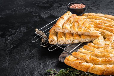 Turkish Tepsi Boregi, Round Borek cheese pie on kitchen board. Black background. Top view. Copy space. clipart