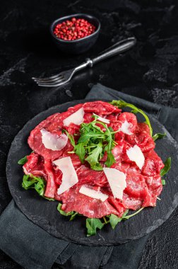 Beef carpaccio with arugula, parmesan cheese. Black background. Top view.