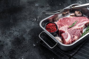 Fresh Raw porterhouse T bone beef meat Steak in steel tray with herbs. Black background. Top view. Copy space.