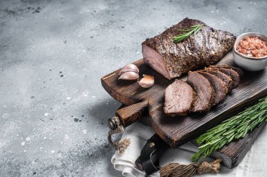 Roast and sliced tri tip beef steak on a wooden board with herbs. Gray background. Top view. Copy space.