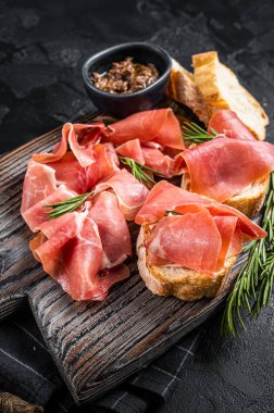 Domatesli tost ve jambonlu jambon dilimleri, ahşap tahtada jambonlu jambonlu jambonlu jambon. Siyah arka plan. Üst görünüm.