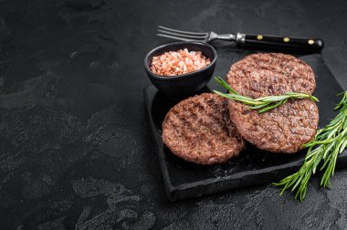 Beef burger patty cutlet for hamburger grilled on BBQ on marble board with rosemary. Black background. Top view. Copy space.