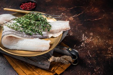 Whitefish fillet, raw Haddock fish on plate with rosemary and thyme. Dark background. Top view. Copy space.