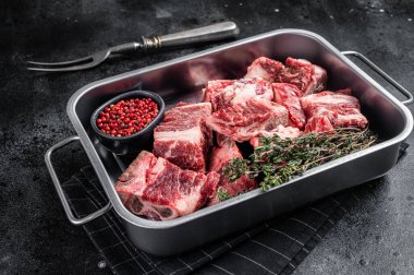 Raw sliced diced beef meat in steel tray with herbs. Black background. Top view.
