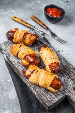 Sausage rolls, Pigs in Blanket puff pastry on wooden board. Gray background. Top view.
