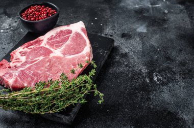 Pork neck steak from raw meat on marble board with herbs. Black background. Top view. Copy space.