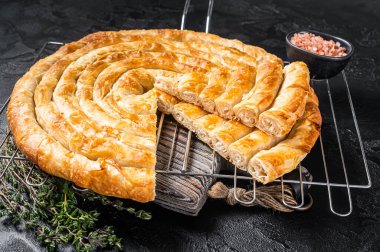 Turkish Tepsi Boregi, Round Borek cheese pie on kitchen board. Black background. Top view.