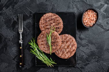 Beef burger patty cutlet for hamburger grilled on BBQ on marble board with rosemary. Black background. Top view.