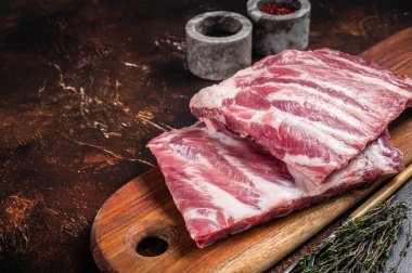 Raw pork spare loin ribs St Louis on wooden board with herbs. Dark background. Top view. Copy space.