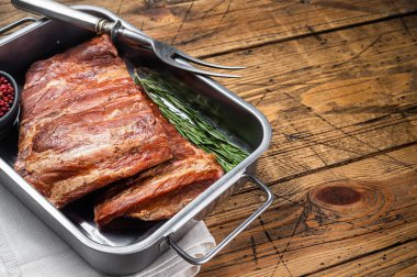 American Smoked Pork spare Ribs in steel tray with herbs. Wooden background. Top view. Copy space.