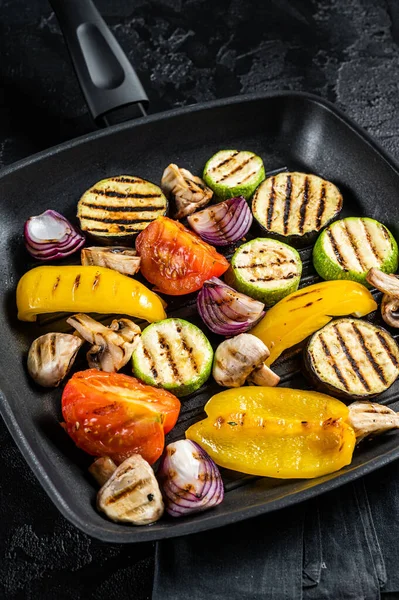 Vegetables grilled in a grill skillet, bell pepper, zucchini, eggplant, onion and tomato. Black background. Top view.