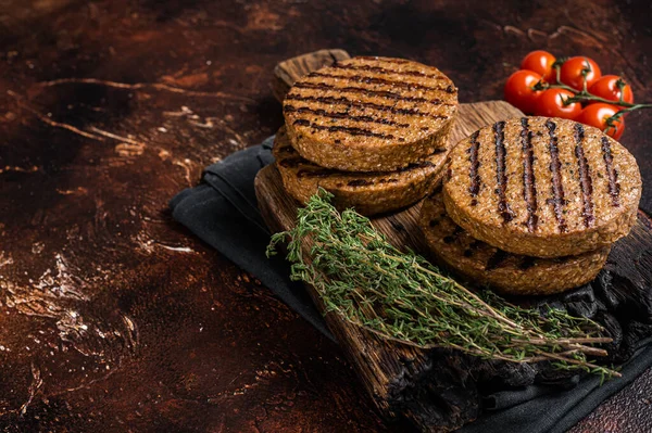 BBQ Grilled plant based meat burger patties, vegan cutlets on wooden board with herbs. Dark background. Top view. Copy space.