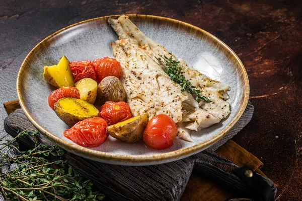 Kavrulmuş Pollock balığı filetosu, garnitür domates ve patatesle birlikte tabakta. Karanlık arka plan. Üst görünüm.