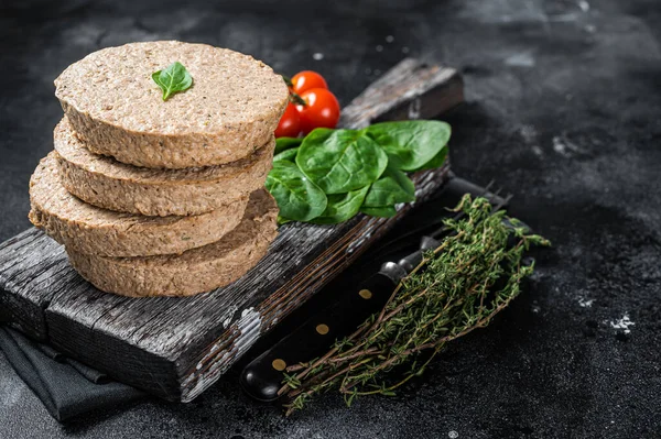 Vegetarian plant based meat burger patties, raw vegan cutlets on wooden board with herbs. Black background. Top view. Copy space.