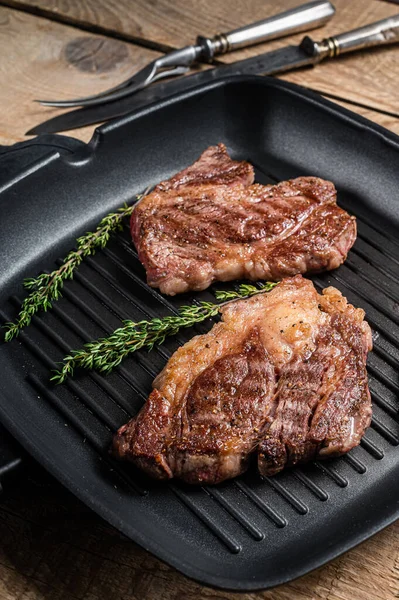 Grilled Chuck eye Roll beef steaks with herbs on grill skillet. Wooden background. Top view.