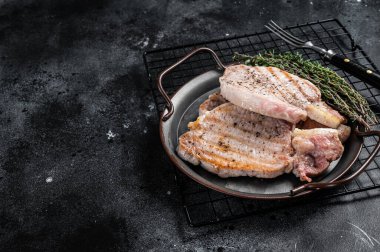 Grilled delicious pork chop steaks with herbs and spices. Black background. Top view. Copy space.