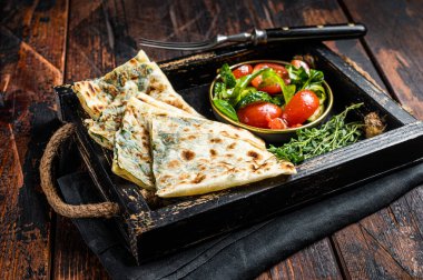 Baked Gozleme flatbread with greens in a box with vegetable salad. Wooden background. Top view.