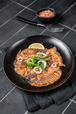 Fresh Salmon carpaccio with onion and arugula on a plate. Black background. Top view.