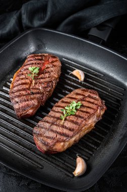 Grilled Top Blade or flat iron roast beef meat steaks on a skillet. Black background. Top View.