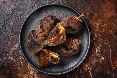 Dried persimmon fruit on a plate. Dark background. Top view.