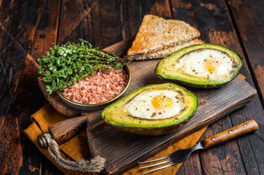 Organic Egg Baked in Avocado with Salt, thyme and Pepper. Dark background. Top view.