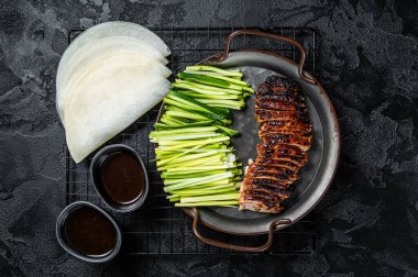 Peking Duck served with cucumber, green onions, and roasted wheaten chinese pancakes with sauce Hoysin. Black background. Top view.
