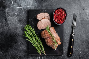Dilimlenmiş bonfile biftek, mermer tahtada rosto ve biberiye. Siyah arka plan. Üst görünüm.
